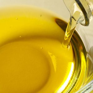 Pouring cooking oil from bottle into bowl on white background, closeup